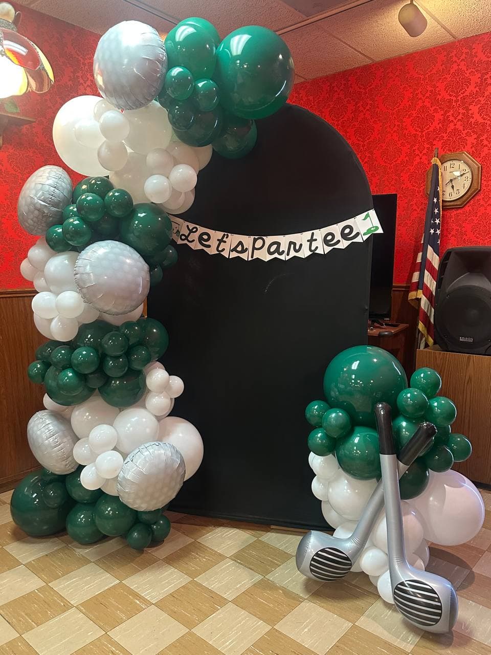 Forest green and white garland with golf club foils around a black arch and a lets par-tee banner